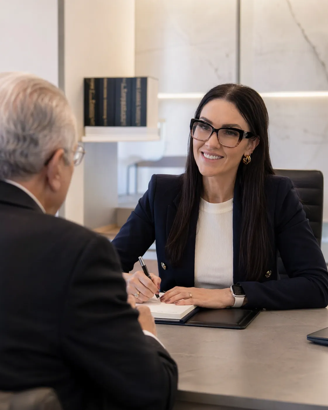 Advogada atende um senhor à mesa e anota as informações dele